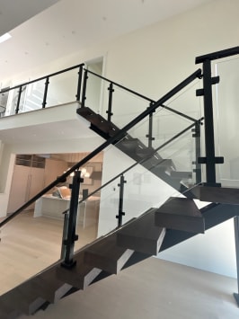 Extra-wide dark wood floating treads on black stringers with black-post glass railing in a bright modern home.