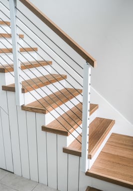 Natural oak treads on a white shiplap stair with white posts, cable infill and a wood cap rail.