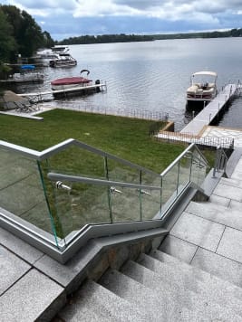 Frameless glass railing on a gray aluminum base rail lines granite steps leading down to a lakeside dock