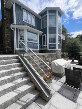Glass base rail railing with a glass-mounted handrail runs up granite steps beside a stone-walled patio