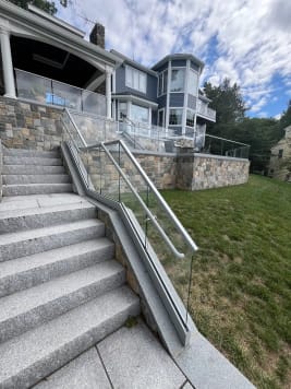 Full run of granite steps lined with glass base rail railing and a glass-mounted handrail below a stone terrace