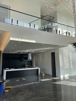 Frameless glass on black talon spigots lines an upper balcony above an open kitchen