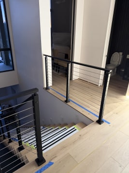Black cable railing guards an oak-floored stair opening with protected treads below