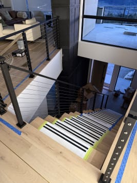 Black-post cable railing follows a stair down from a loft to the main floor