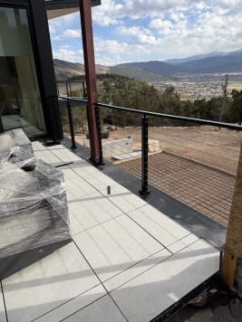 Black cable railing on a tiled deck overlooking a valley town and distant mountains