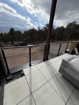 Black cable railing on a tiled deck above a wooded hillside