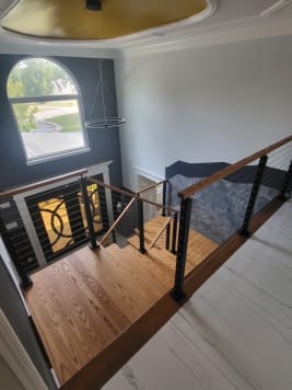 Oak landing and black cable railing seen from above in a two-story foyer with an arched window