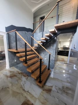 Switchback floating oak stair with black cable railing above a glossy marble floor