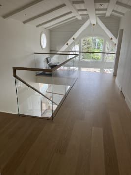 Frameless glass with a wood top cap wraps a stair opening under a white vaulted ceiling and arched window