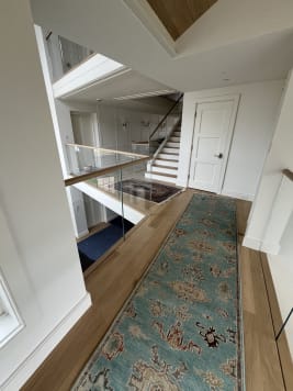 Frameless glass and wood top cap guard a stair opening beside a patterned runner