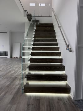 Dark wood cantilever treads with LED lighting, frameless glass on standoff pins and a stainless wall handrail