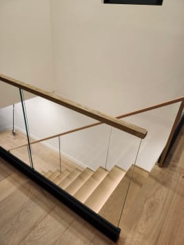 Frameless glass in a black base rail with a white oak top cap at a stair opening