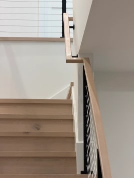 Oak stair treads with black cable railing and a white oak handrail turning at a landing