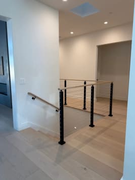 Black cable railing with white oak cap guards a stair opening on pale oak floors