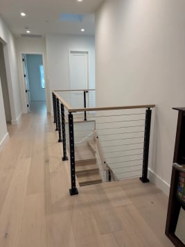 Cable railing with black posts and oak cap around a stair opening in an upstairs hall