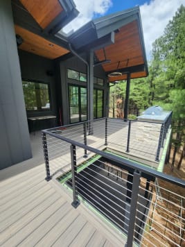 Two levels of black cable railing on a dark modern home set in a pine forest