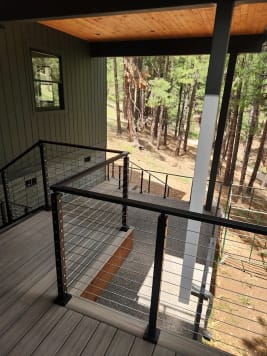 Black cable railing frames a covered balcony above a pine-forested hillside
