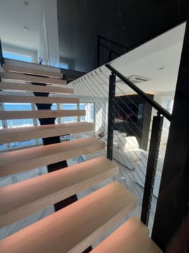 Thick maple floating treads on a black mono stringer with LED lighting and black cable railing