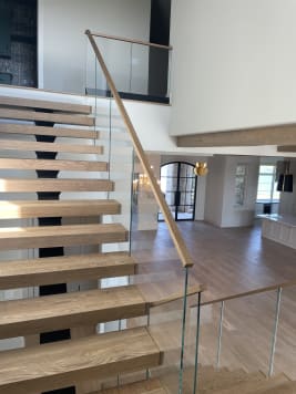 Floating oak treads on a black mono stringer with Vedera glass and wood handrail in an open great room