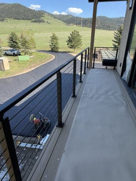 Black cable railing along a covered balcony overlooking green hills