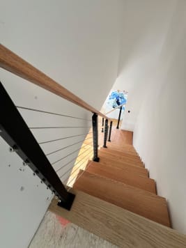Looking down red oak floating treads with black cable railing and oak handrail