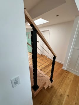 Black cable railing and oak handrail at the base of a floating stair