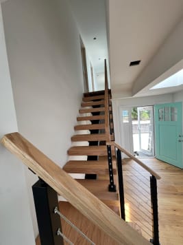 Straight red oak floating stair with black cable railing and oak handrail toward a turquoise front door
