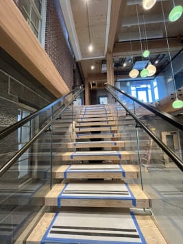 Wide floating stair with frameless glass and black handrails rising through a mass-timber commercial atrium