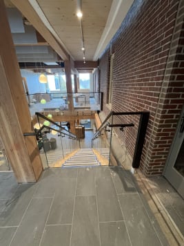 Frameless glass with black handrails around a stair opening beside exposed brick and timber columns