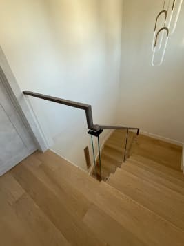 Frameless standoff-pin glass and dark wood handrail at the top of a white oak stair
