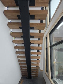 Black mono stringer with thick oak treads seen from below beside tall windows