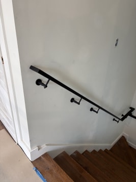 Black steel wall-mounted handrail descending a dark-tread stair