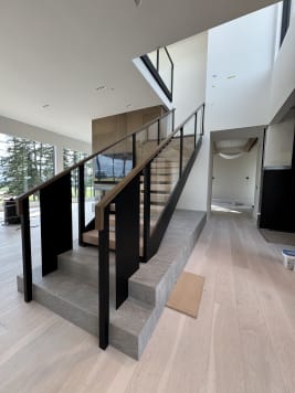 Twin black steel plate stringers and glass railing with walnut handrail on a stone-plinth stair