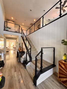 Black post glass railing runs up a stair and across the loft of a bright two-story entry
