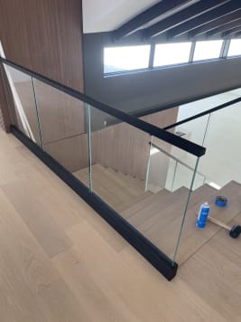 Black base rail glass with a black cap edges a stair opening beside a walnut-paneled wall