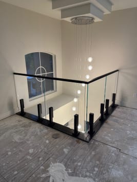 Frameless glass on black talon spigots with a black cap wraps a loft beside a cascading crystal pendant and arched window