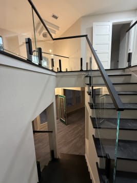 Frameless glass on black talon spigots runs up a dark-tread stair to a vaulted loft