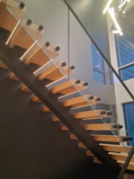 White oak floating treads with LED strips on a black mono stringer beside frameless glass and a black handrail