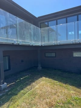 Frameless glass on side-mount brackets wraps an elevated deck on a gray modern home above a lawn