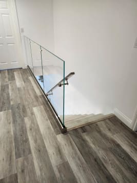 Frameless glass in a stainless base rail with a stainless wall handrail at the top of a stair