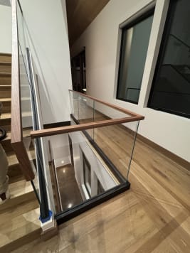 Frameless base rail glass with a mitered walnut cap wraps a stairwell on wide oak floors