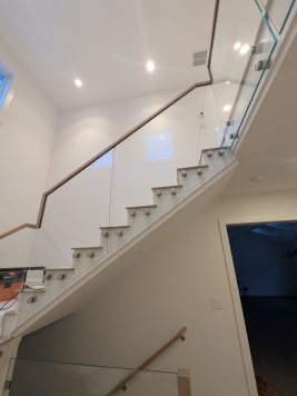 Glass panels fixed with stainless standoff pins to the stair stringer, topped by a light wood handrail.