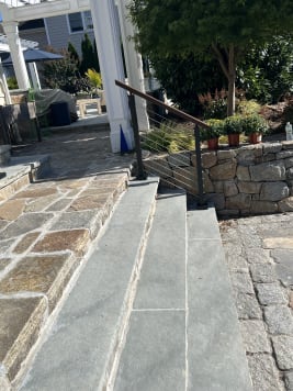 Black cable railing with a wood handrail runs beside bluestone steps leading to a stone patio.