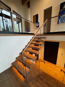 Oak floating treads with LED under-lighting turn at a landing beneath a glass balcony guard with wood handrail.
