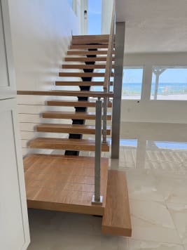 Oak treads on a black center stringer rise past stainless cable railing toward ocean-view windows.