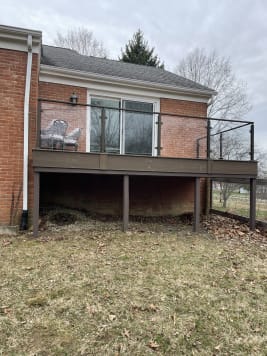 A raised composite deck on a red brick home is enclosed by dark posts with glass panels.