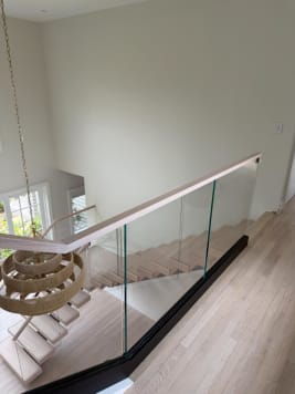 Looking down past a base-rail glass guard with oak handrail onto white-oak floating treads and a woven pendant.