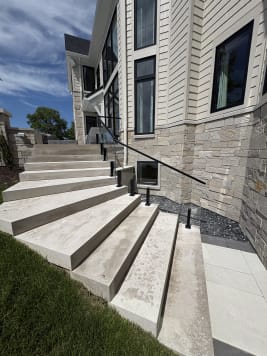 Black talon clamps hold frameless glass with a black top rail along sweeping limestone exterior steps beside a stone-clad home.