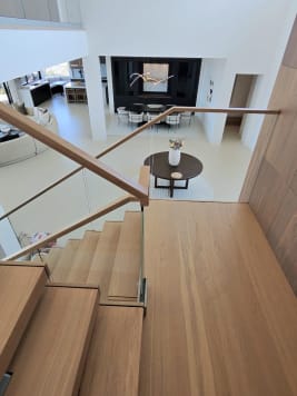 White oak floating treads with glass railing and wood handrail descend into an open modern living space.