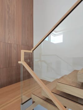 Glass panel with a white oak handrail beside thick floating oak treads against a walnut wall.